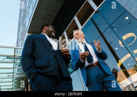 Multiracial men dressed in suits talking and gesturing while going down stairs outdoors Stock Photo