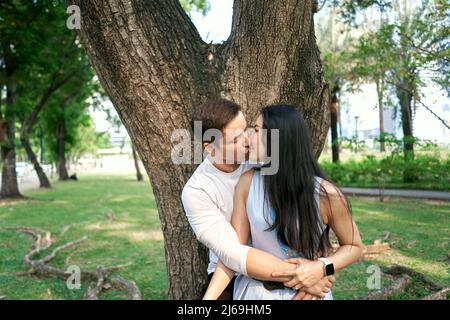 Multiethnic couple embracing while kissing in a park Stock Photo