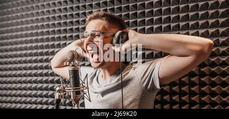 The vocalist sings in the studio in a microphone. Man in headphones writes a podcast, an audiobook. Artist, recording an album, working with the label Stock Photo