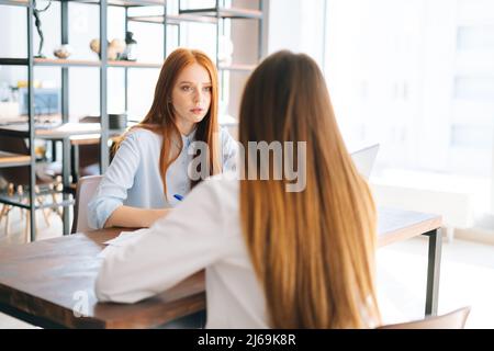 Back close-up view of unrecognizable woman applicant being interviewed by serious female HR managers reading resume Stock Photo