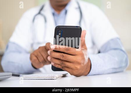 close up shot of doctor using mobile phone while at hospital - concept of virutal doctor consultation , taking break and healthcare service. Stock Photo