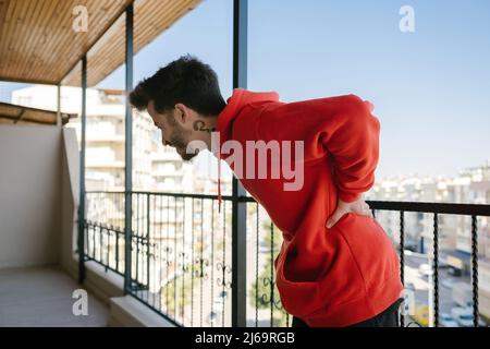 Image of man suffering back pain. Young man wearing red hoodie lower back painful injury. Pain concept. Stock Photo