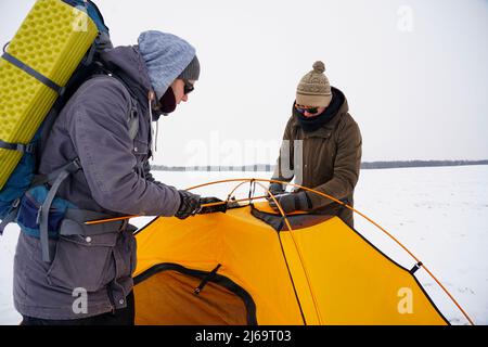 Two guys are setting up a tent in the snow. Setting up a tent during a winter expedition in extreme conditions. Winter trekking Stock Photo