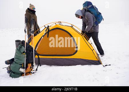 Two guys are setting up a tent in the snow. Setting up a tent during a winter expedition in extreme conditions. Winter trekking Stock Photo