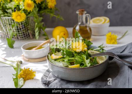 Dandelion salad with olive oil, lemon juice and spices on white wooden table with grey background Stock Photo