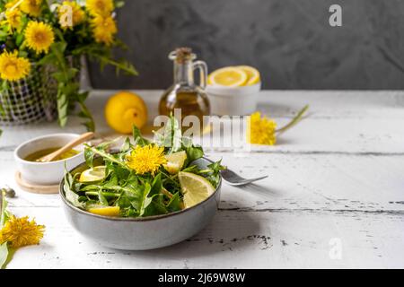 Dandelion salad with olive oil, lemon juice and spices on white wooden table with grey background. Copy space Stock Photo