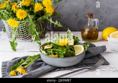 Dandelion salad with olive oil, lemon juice and spices on white wooden table with grey background Stock Photo