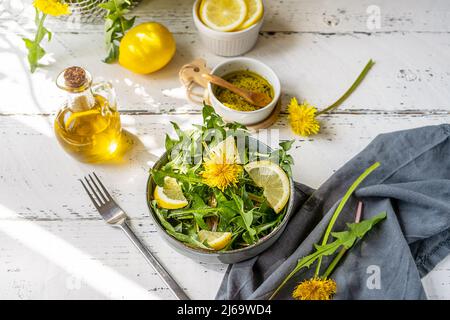 Dandelion salad with olive oil, lemon juice and spices on white wooden table with grey background Stock Photo
