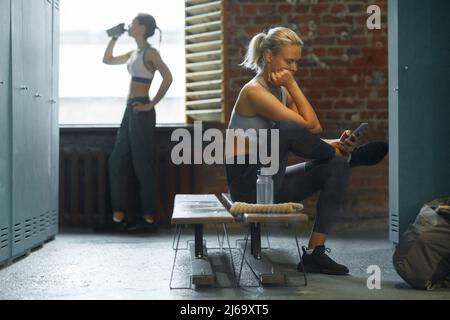 Two relaxed young women spending break time in gym dressing room horizontal shot Stock Photo