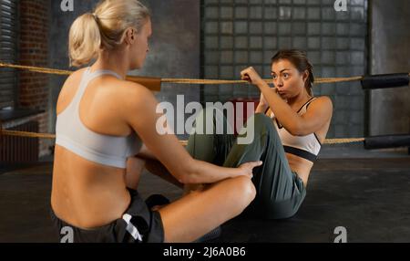 Blond woman helping her friend to do boxing exercise on squared ring horizontal shot Stock Photo