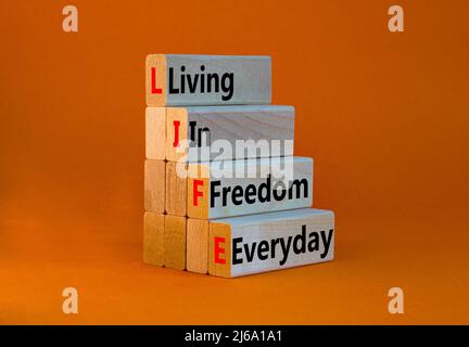 LIFE living in freedom everyday symbol. Concept words LIFE living in freedom everyday on wooden blocks on a beautiful orange background. Business LIFE Stock Photo