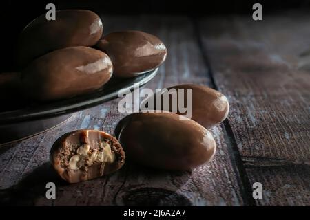 Milk chocolate covered nuts on a black plate and over a rustic wooden table macro dark food photography horizontal side view shot Stock Photo