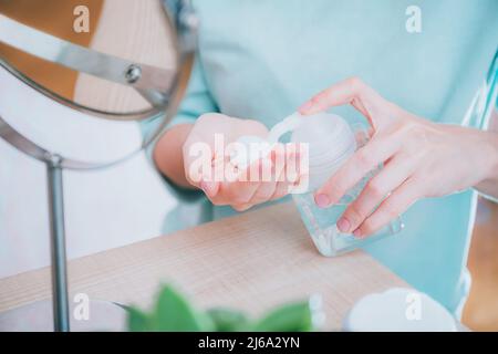 Girl squeezes skin care product from dispenser into the palm in front of the mirror. Skin care, facial skin cleansing with foam, natural cosmetics Stock Photo