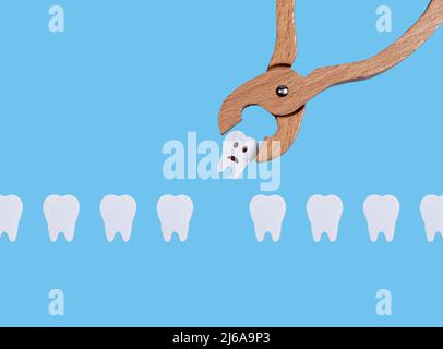 Teeth row and dental forceps. Pulling bad sick tooth with sad emoji because of decay, periodontal disease. Oral health and dentist work concept on blue background. Children game at doctor. photo Stock Photo