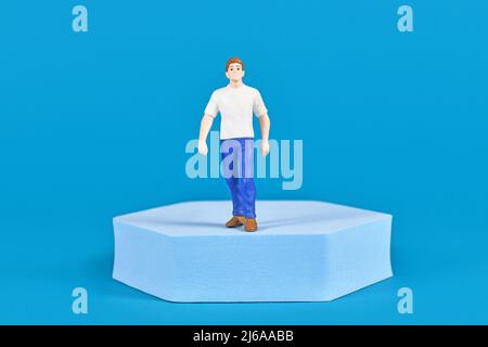 Man figure with shirt and jeans on pedestal in front of blue background Stock Photo
