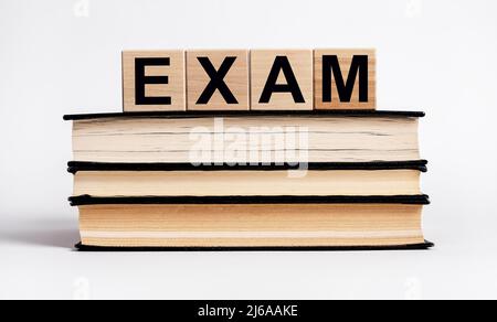 Word exam on Books stack with wooden blocks. Preparation for examination, education concept. Data learning by reading. Getting knowledge from textbook. Stock Photo