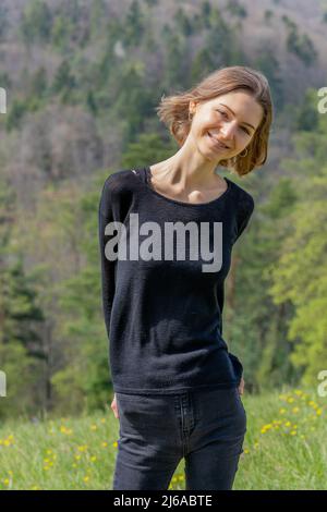 Portrait of young beautiful woman wearing black clothes smiling at camera in nature of Switzerland in springtime. Stock Photo