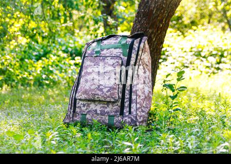 Defocus military backpack. Army bag on green grass background near tree. Military camouflage webbing material on a British army rucksack, backpack. To Stock Photo