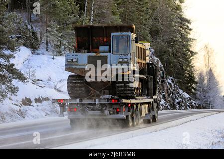 Black Volvo FMX truck Lonnqvist Oy hauls Hitachi CG 110 tracked dumper on flatbed trailer on highway 52 in winter. Salo, Finland. December 28, 2021. Stock Photo