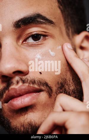 Close-up of young mixed race man applying cream on his face Stock Photo