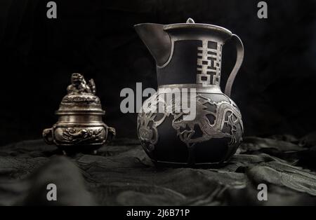 Chinese antique teapot (Characters chinese is Double Happiness) in frot of Silver antique incense burner on dark background. Chinese traditional style Stock Photo