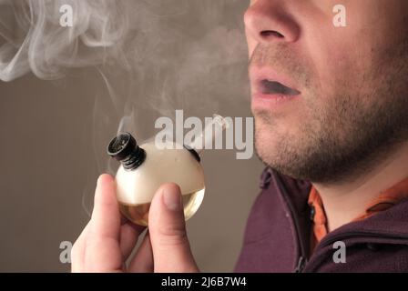 Smoking medicinal marijuana. Weed smoker's close-up portrait with a lot of fume. Young man smoking CBD cannabis with a bong. Marihuana effect for medi Stock Photo