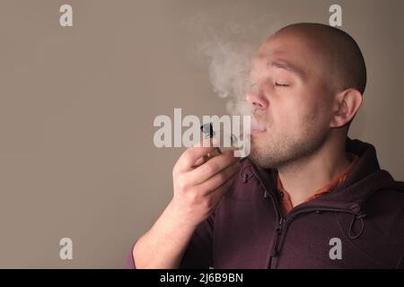 Smoking medicinal marijuana. Young man smoking CBD cannabis with a bong. Weed smoker's close-up portrait with a lot of fume. Marihuana effect for medi Stock Photo