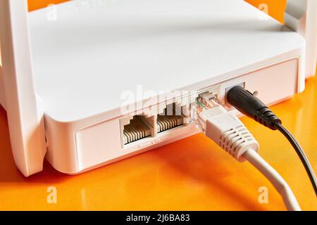 White wireless router on orange background connected by cable to the Internet. Close-up Stock Photo