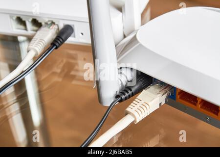 Two white wireless routers on a glass table connected by cables to the Internet. Close-up Stock Photo