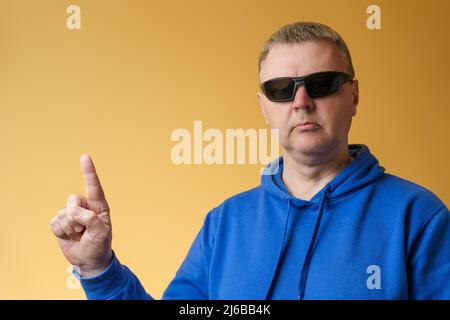 The European points with his finger. Portrait of a man in a blue hoodie and sunglasses. Stock Photo