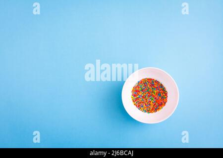 White pbowl with colorful sugar sprinkles on blue background with free copy paste space. Stock Photo