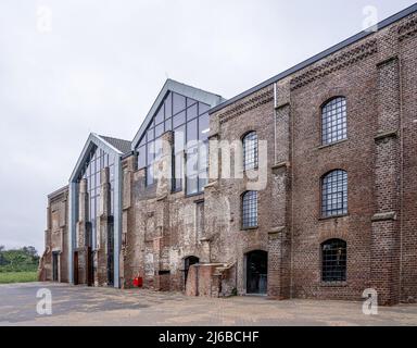 Dark brick facade of an old abandoned factory. The stones are damaged and outdated, but new windows have been installed so that the restored building Stock Photo