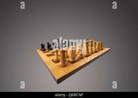 White and black chess pieces with the white pieces in the foreground are placed on a chessboard. The board and the pieces are isolated in a gray space Stock Photo