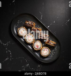 Hot fried sushi rolls and maki with shrimp , cream cheese, avocado and wasabi on black stone, selective focus. Japanese kitchen. Deep-fried. Sushi men Stock Photo