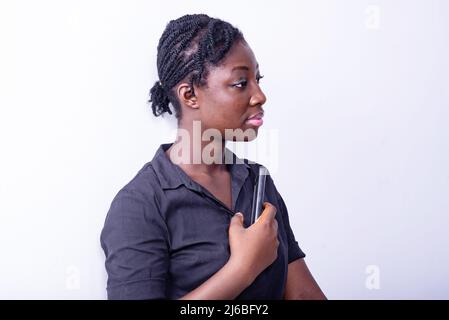 a young female student standing on white background holding cellphone looking away Stock Photo