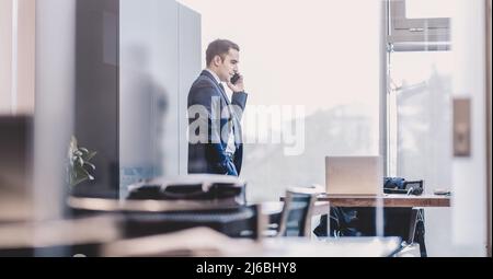 Businessman talking on a mobile phone while looking through window. Stock Photo