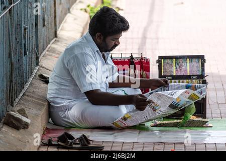 Vellore, Tamil Nadu, India - September 2018: An Indian fortune teller wearing a white shirt sitting beside his pavement shop and reading a newspaper. Stock Photo