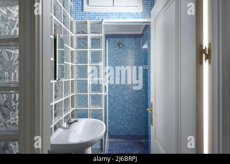 Bathroom with white porcelain sink with glass paves brick walls, blue tiled shower stall and white millwork Stock Photo