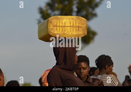 A young woman with a jerrycan of water on her head, coming from fetching lake water. Stock Photo