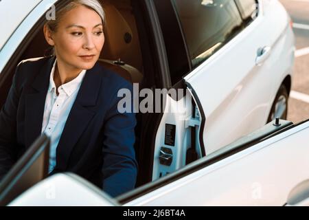 Mature asian businesswoman with grey hair getting out car Stock Photo