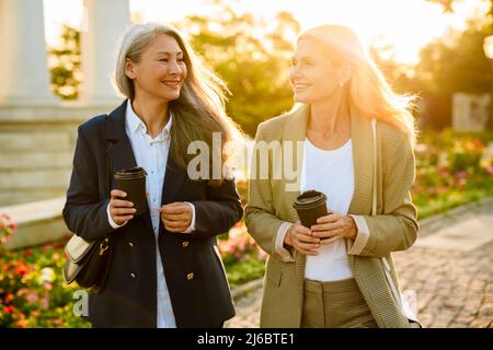 Mature multiracial businesswomen drinking coffee during walking outdoors Stock Photo