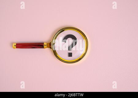 Question mark under magnifying glass, on pink background Stock Photo