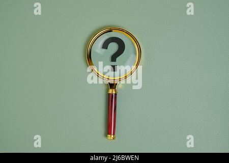 Question mark under magnifying glass, on green background Stock Photo