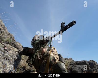 An ambush in mountains - professional special forces sniper during a special operation aiming at the enemy. Concept of modern military operations and Stock Photo