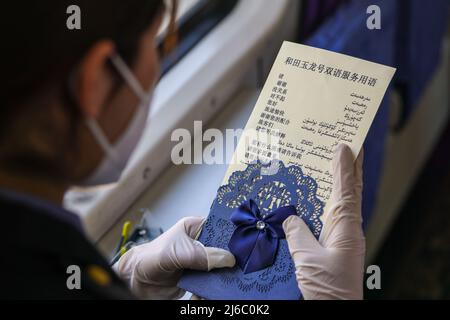 (220430) -- KASHGAR, April 30, 2022 (Xinhua) -- A train attendant studies the reference for Uygur language and Mandarin Chinese translation aboard a slow train running in northwest China's Xinjiang Uygur Autonomous Region, April 29, 2022.  As bullet trains zoom through stations in many parts of China, the seemingly outdated, rumbling slow-speed trains have continued to serve residents of remote areas with stable ticket prices and services.   Though home to the world's most developed high-speed railway network, China still regularly operates 81 slow train services. The trains 7556/7557 and 7558 Stock Photo