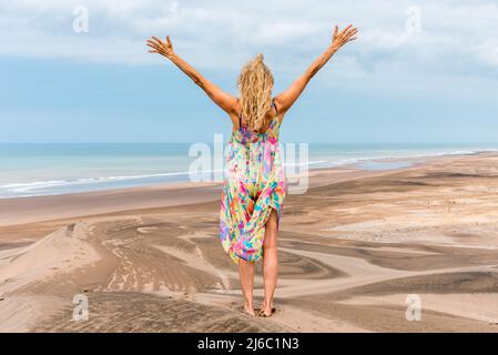 Back of a blonde woman standing on the desert gesturing freedom with the arms while facing the sea. Stock Photo