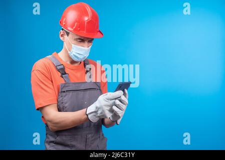 Male builder in face mask browsing social media on smartphone Stock Photo