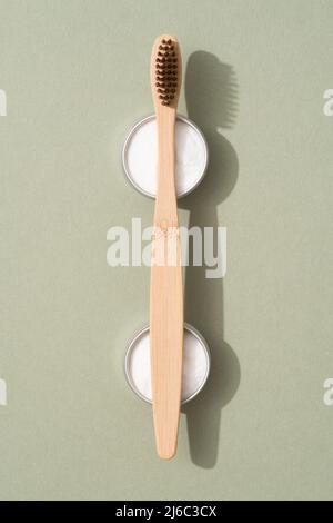 Wooden bamboo toothbrushes with natural bristle and mineral toothpowder kaolin in metal containers on green background. Natural bath products, organic Stock Photo