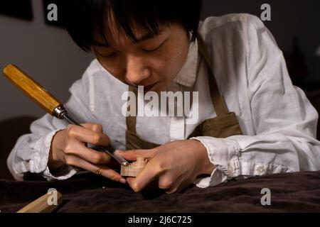 young Chinese female violin maker working with gouge to making a new violin in her workshop Stock Photo