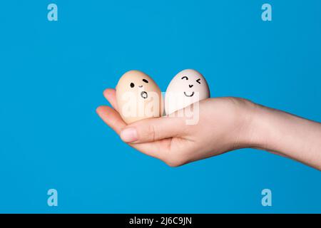 Hand holding two easter eggs with a funny face drawn on it. Easter or healthy diet eating concept Stock Photo